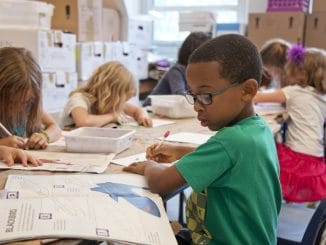 boy in green sweater writing on white paper