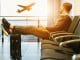 man sitting on gang chair with feet on luggage looking at airplane