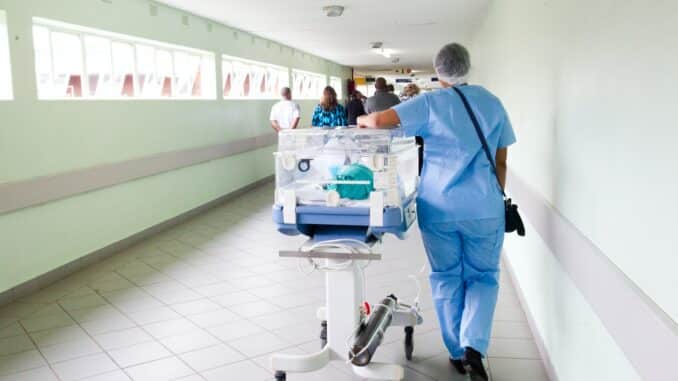 person walking on hallway in blue scrub suit near incubator